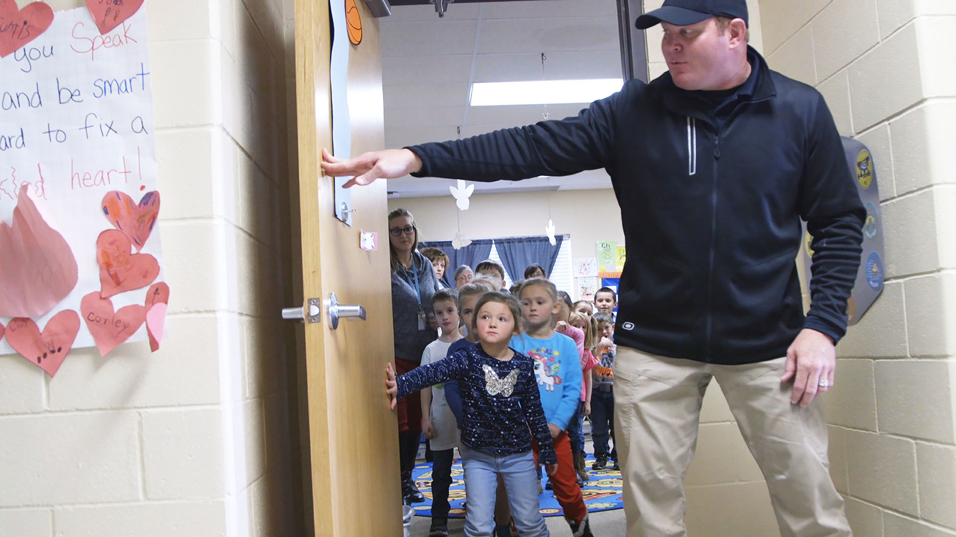 A young student helps the trainer hold a door open as her class practices an evacuation drill.